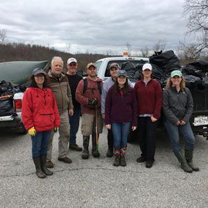 Group of hikers in outdoor gear posing beside a vehicle loaded with supplies on a cloudy day