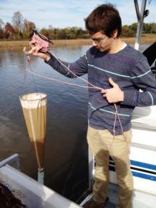 Person holding a fish over a funnel in a body of water, with ropes and a measuring container below