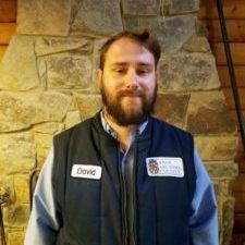 Man standing indoors before a stone wall, wearing a blue vest and name tag reading “David.”