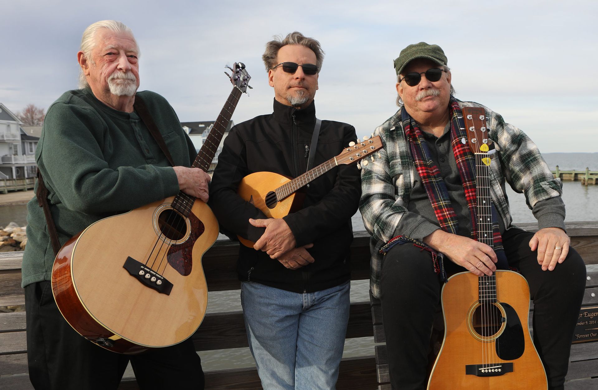 Three musicians posing outdoors by the water with acoustic guitars