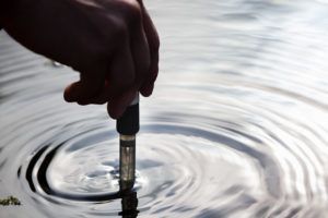 Hand holding a test probe in rippling water to measure water quality