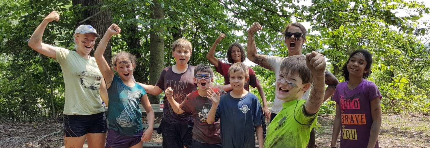 Group of smiling people outdoors in a wooded area, raising their arms and posing together.