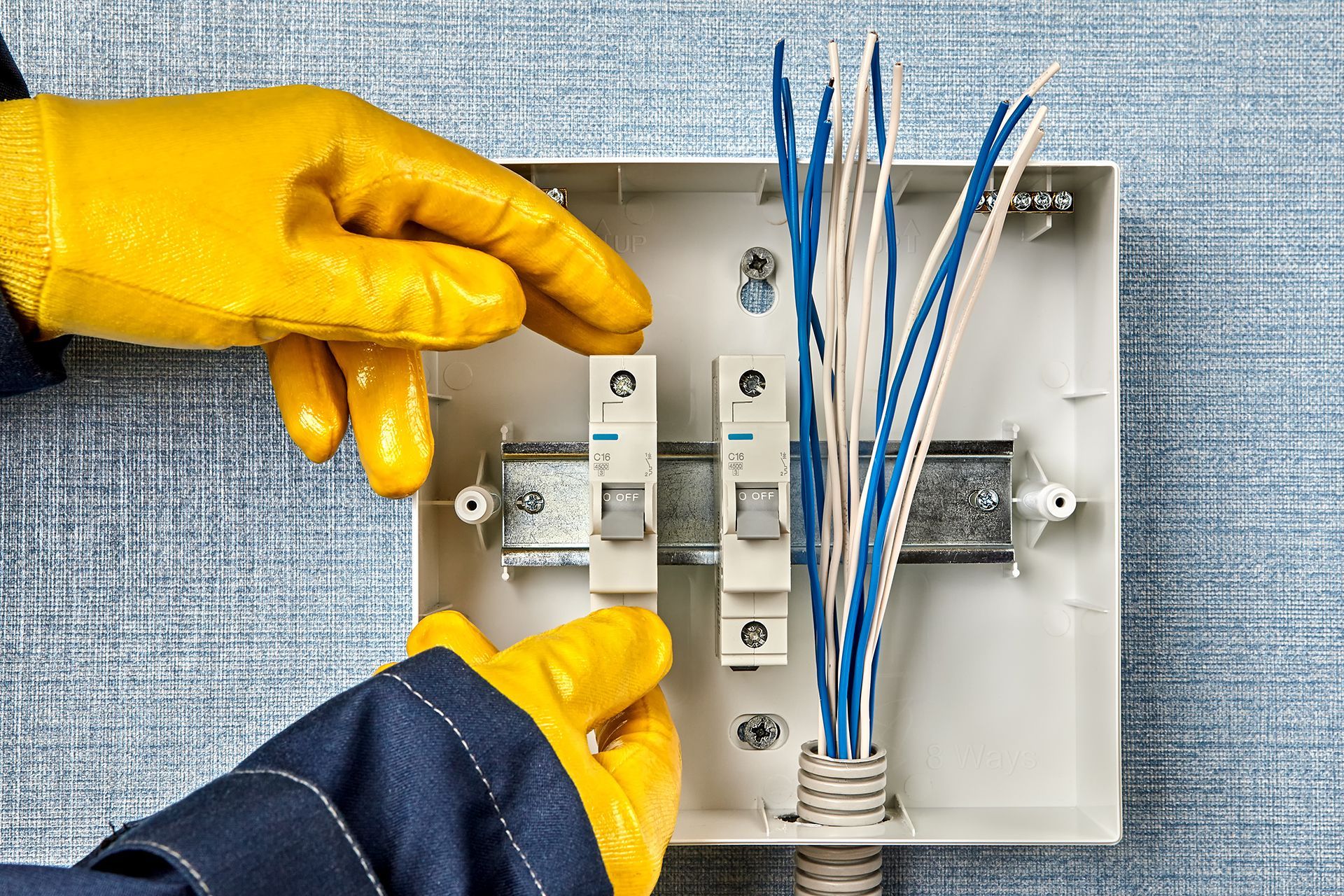 A person wearing yellow gloves is working on an electrical box