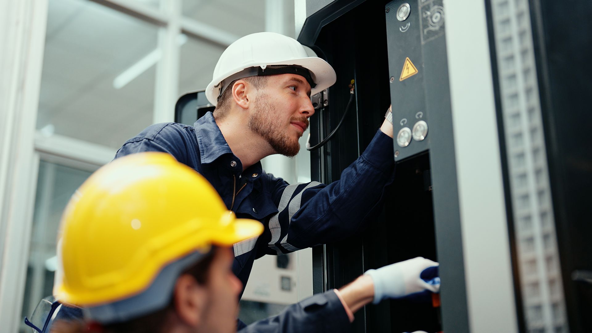 Two men wearing hard hats are working on a machine