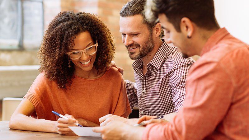 two men and a woman smiling over a piece of paper