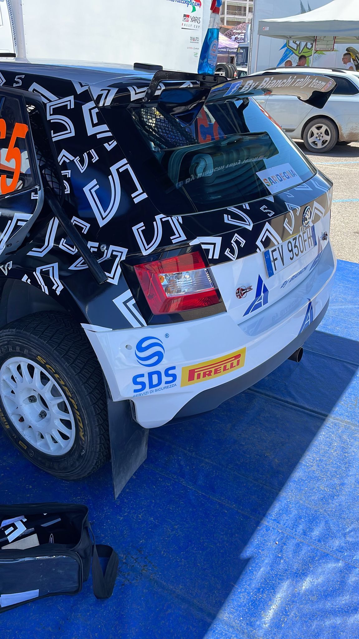 Vista posteriore di un'auto da rally bianca e nera con i loghi degli sponsor su una superficie blu.