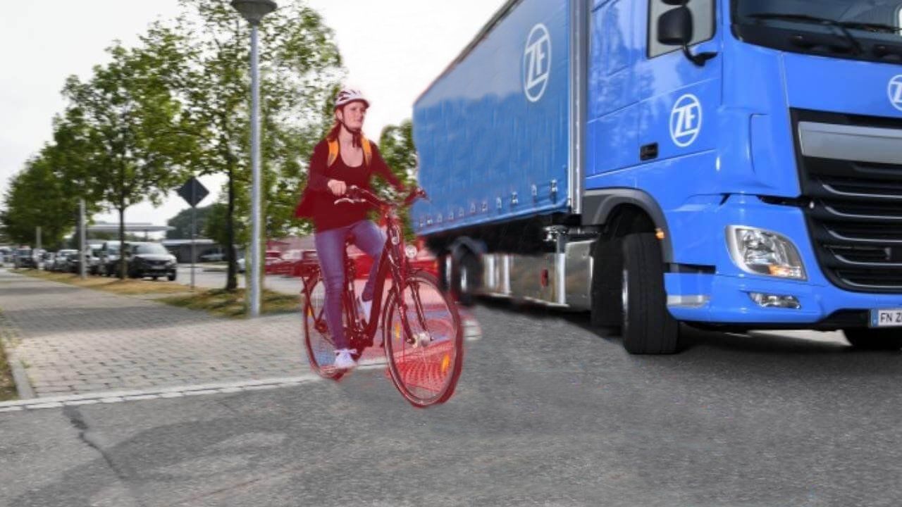 Donna su una bicicletta rossa accanto a un grande camion blu. Scena di strada, indossa un casco.