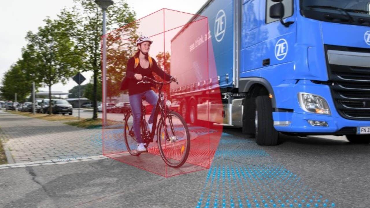 Donna in bicicletta nella zona di allerta rossa di un camion blu su una strada cittadina.