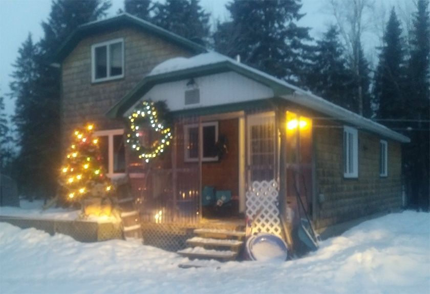 Maison avec lumières de Noël et neige ; couronne sur le porche, arbre illuminé à côté du porche.