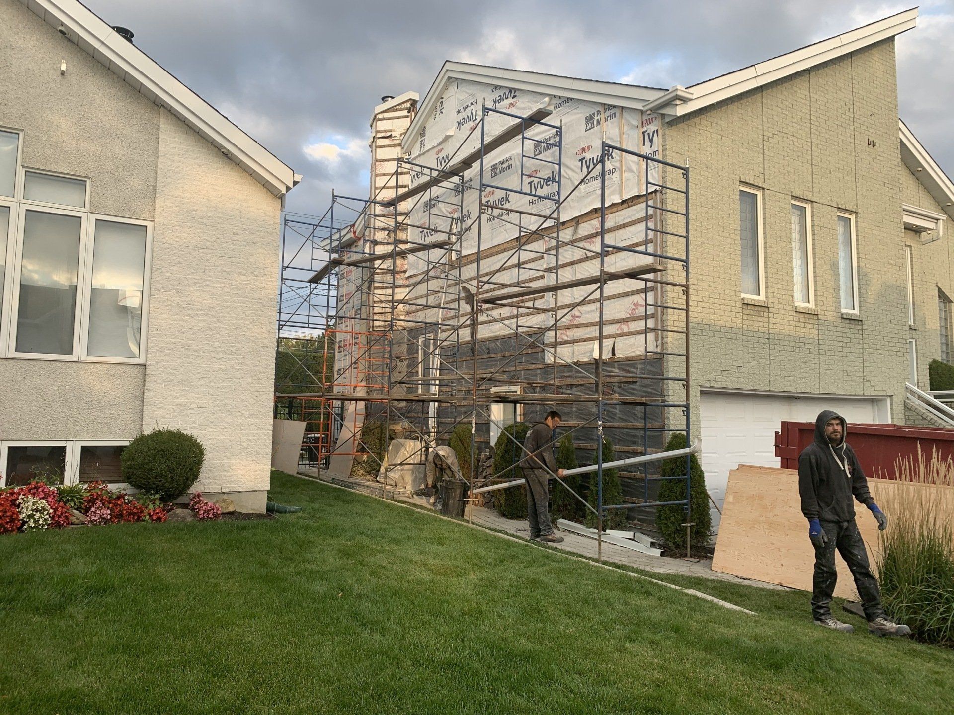 Des ouvriers du bâtiment sur un échafaudage rénovent un bâtiment avec un revêtement beige et clair.