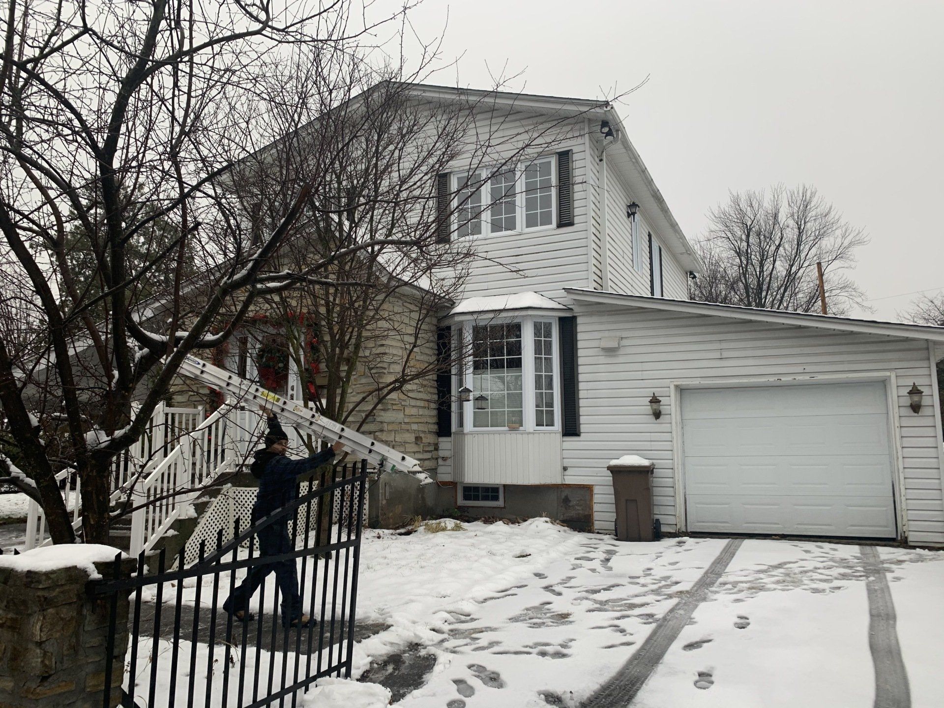 Une personne portant une échelle près d'une maison blanche dans des conditions de neige.