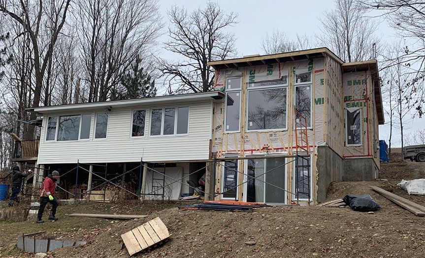 Maison en construction, partiellement construite avec une extension. Personne à proximité. Vue extérieure, journée nuageuse.