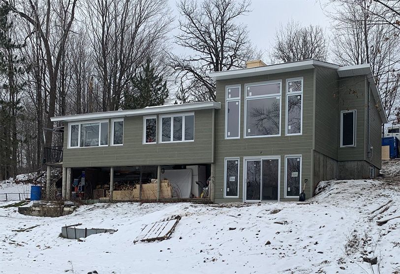 Une maison à deux étages avec de grandes fenêtres, un revêtement vert clair et une cour enneigée.