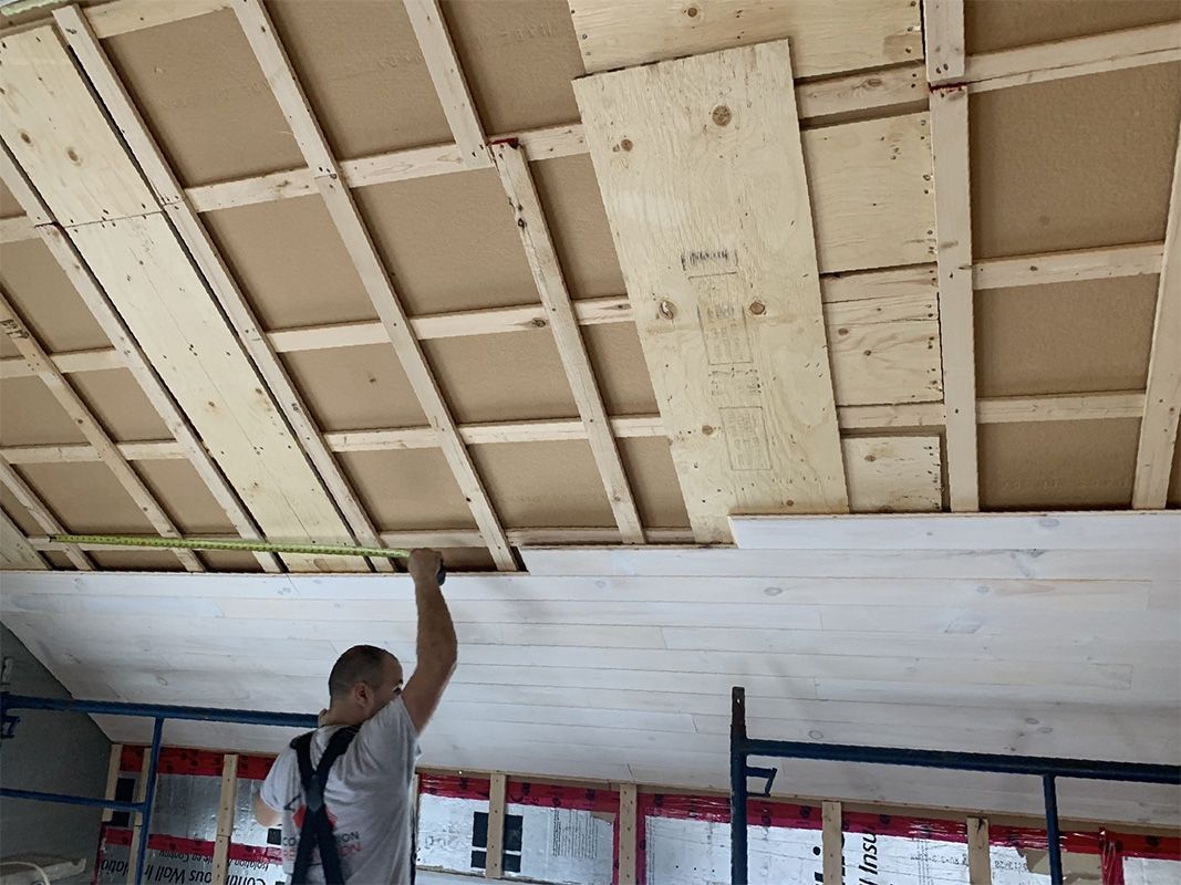 Un homme installe des cloisons sèches au plafond, ossature bois visible. Aménagement intérieur avec isolation.