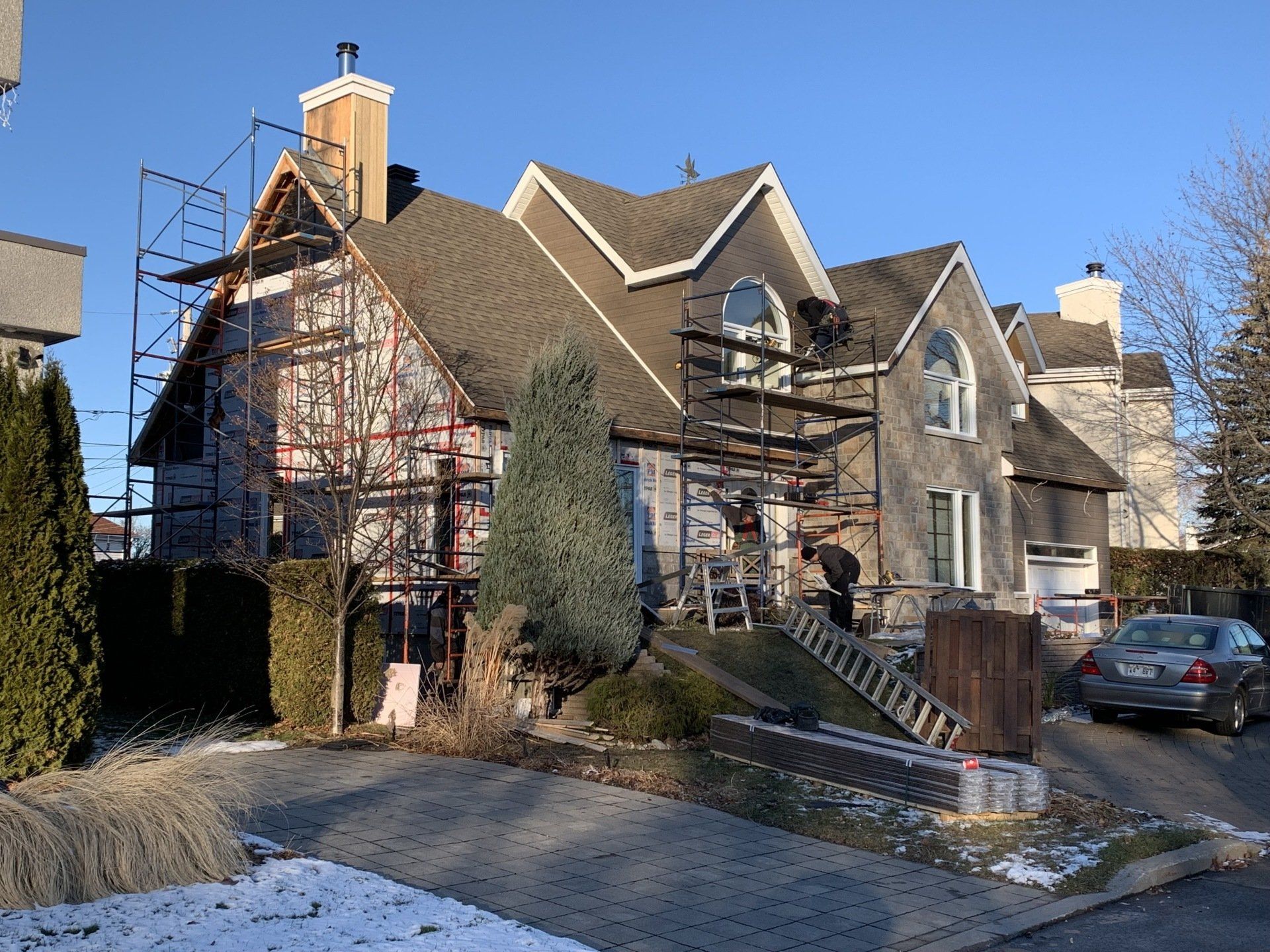 Extérieur d'une maison en rénovation, recouverte d'échafaudages. Scène hivernale avec neige au sol, journée ensoleillée.