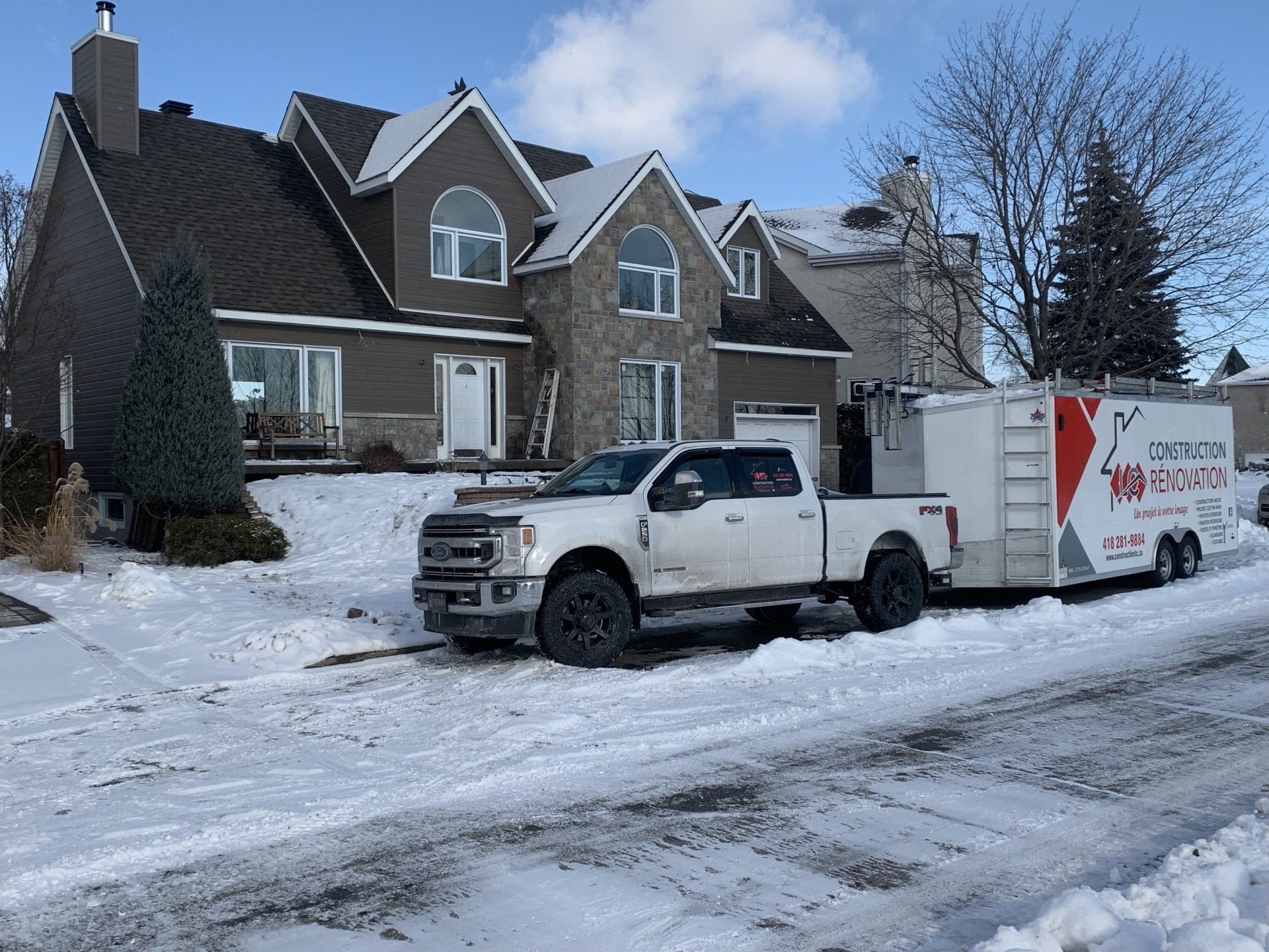 Camion blanc et remorque garés devant une maison recouverte de neige.