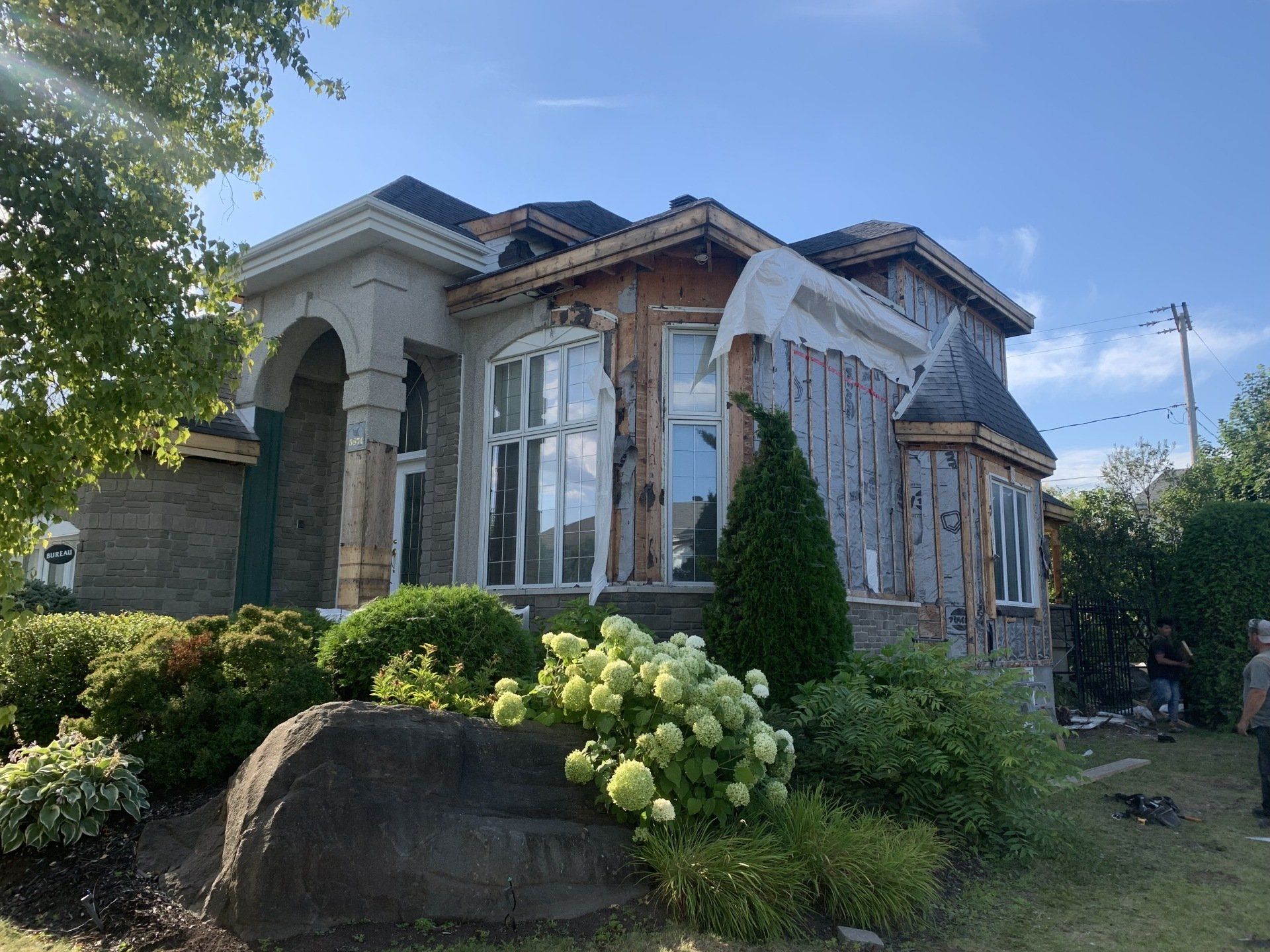 Maison en cours de rénovation avec charpente apparente, entourée de verdure.