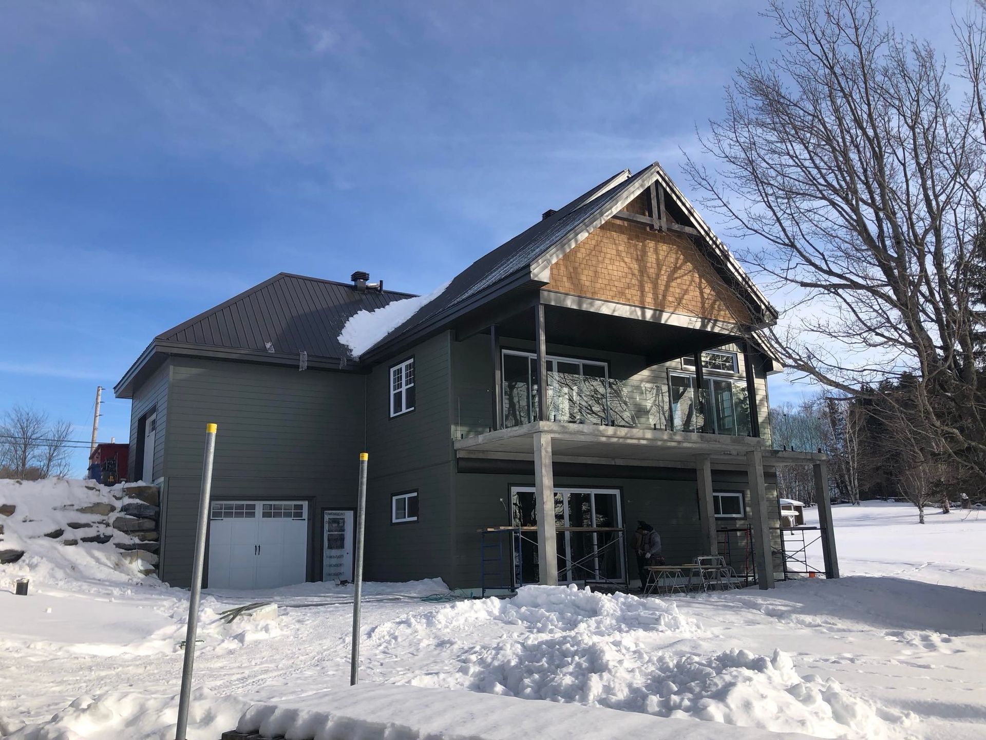 Maison à deux étages en hiver avec neige, revêtement vert et balcon, sous un ciel bleu.
