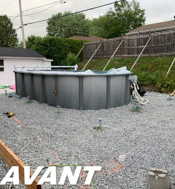 Piscine hors sol en construction dans une cour en gravier avec clôture et bâtiments environnants.