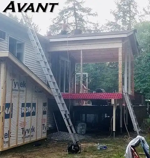 Chantier : maison avec terrasse en bois en construction. Ouvriers sur le toit et au sol, échelles présentes.