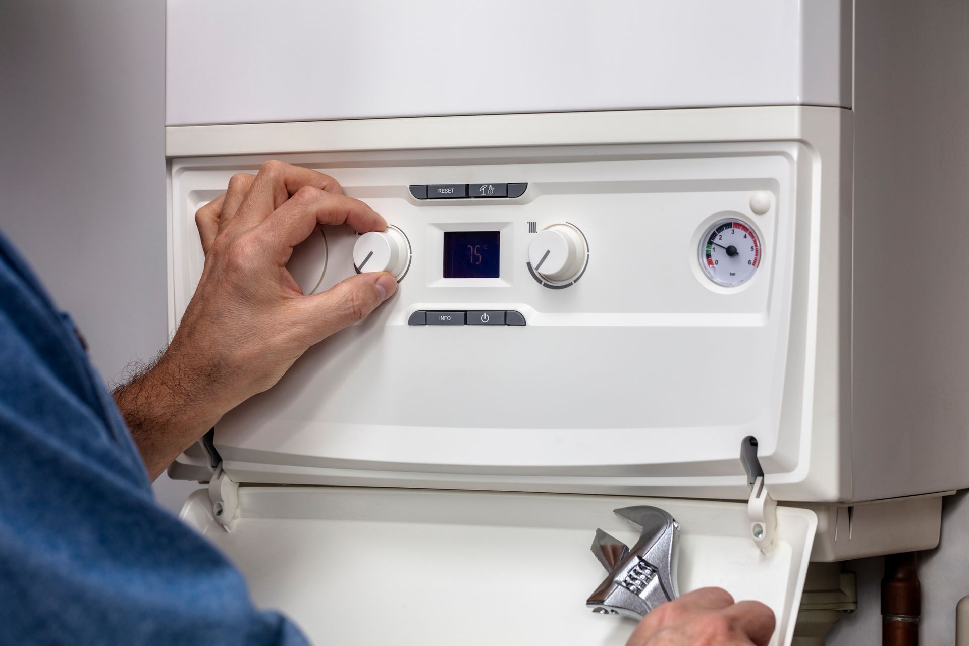 Person adjusting the dial on a white boiler, wrench in hand.