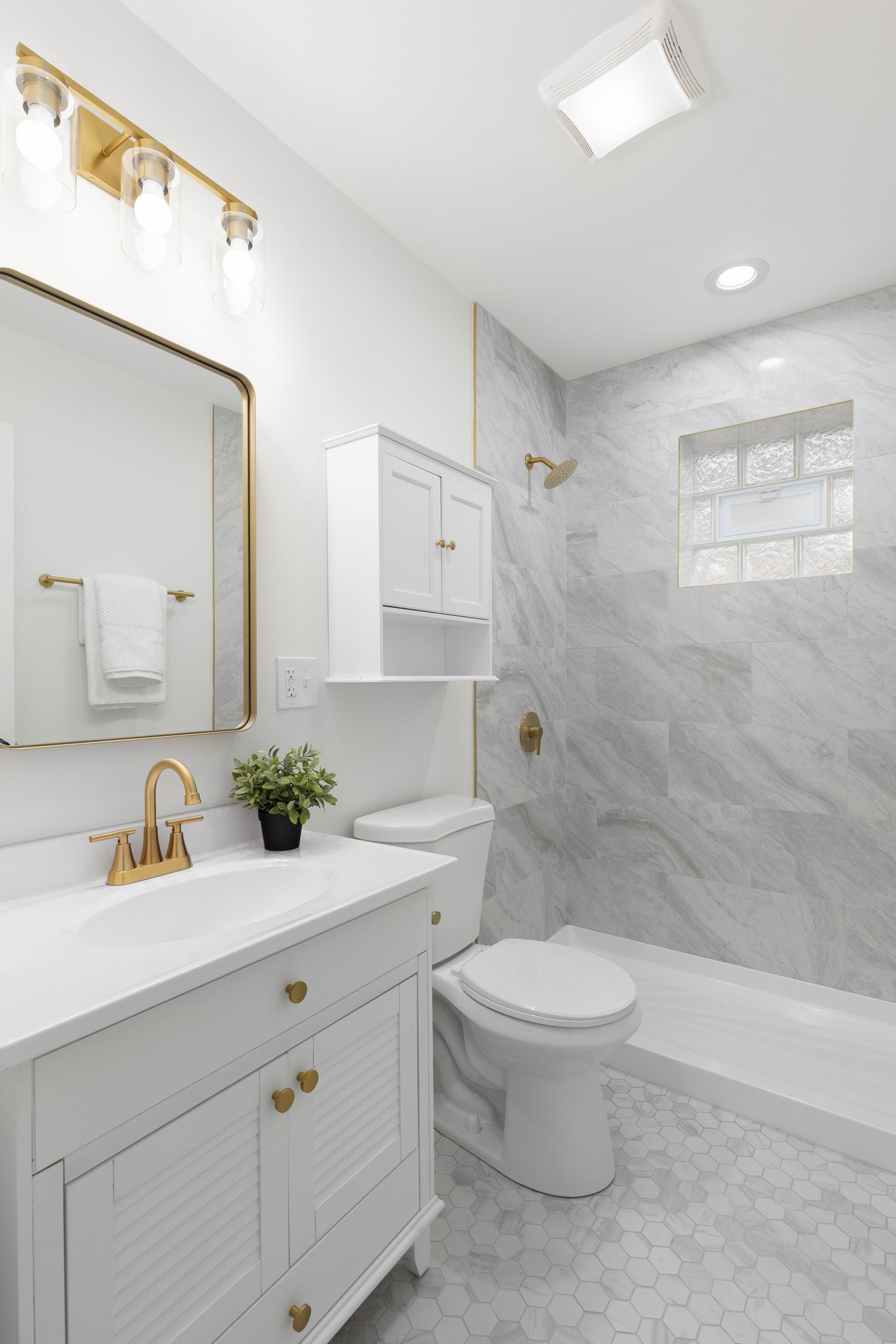 White bathroom with marble shower, gold fixtures, and white vanity.