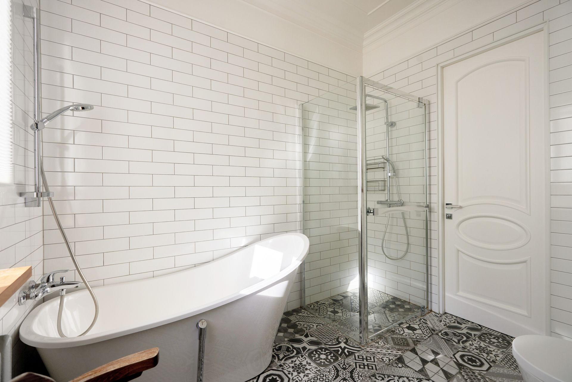 White bathroom with a curved tub, glass shower, and patterned floor.