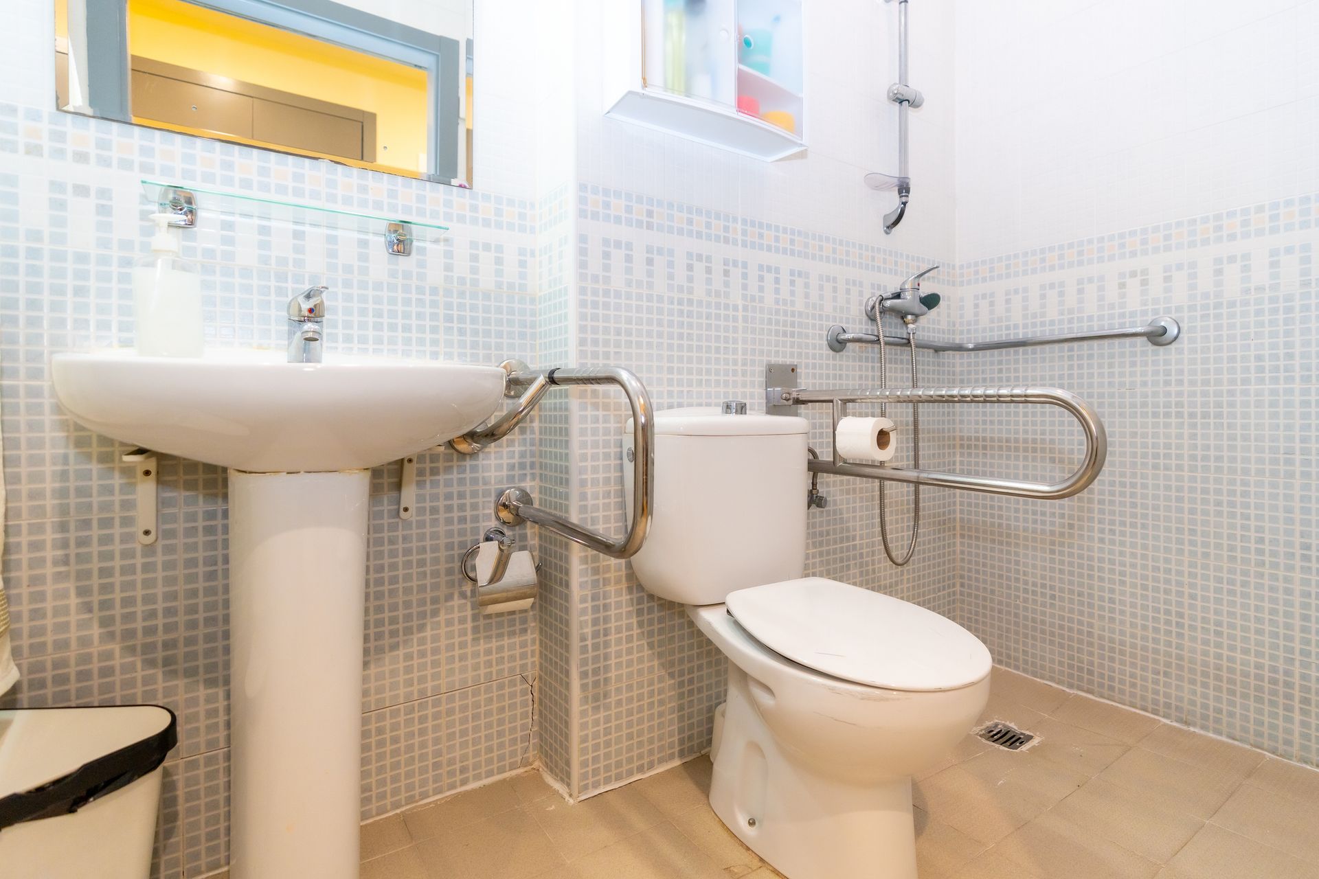 Accessible bathroom with toilet, sink, and grab bars. Light blue tiled walls and white fixtures.