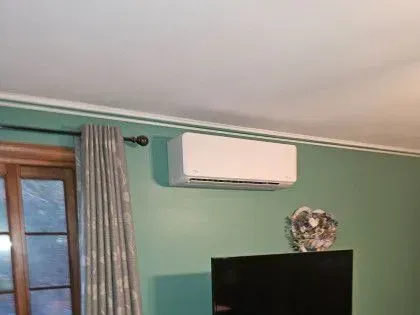 Living room corner with wall-mounted air conditioner, curtain, and TV against a green wall.