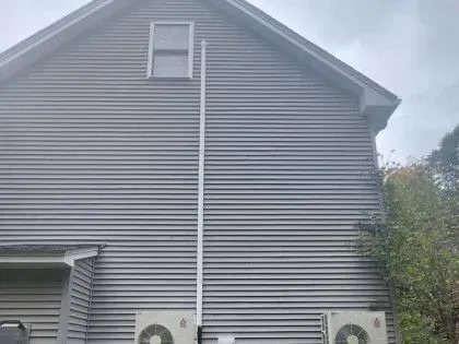 Gray-sided house exterior with a steep gable roof, small upper window, and utility meter below.