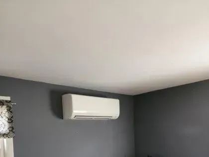 White wall-mounted air conditioner on a dark gray room wall near the ceiling.