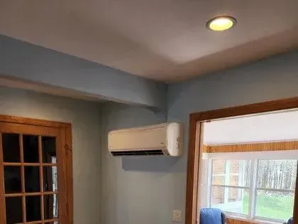Empty room with blue walls, ceiling light, wall AC unit, and a window by a wooden door