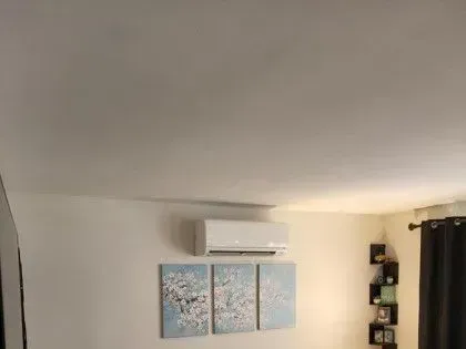 White living room wall with air conditioner and three-panel blue abstract artwork above a dark curtain.