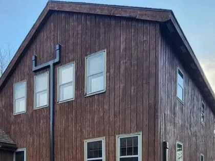 Brown wooden barn with white-trimmed windows and a black cross sign on the upper left side