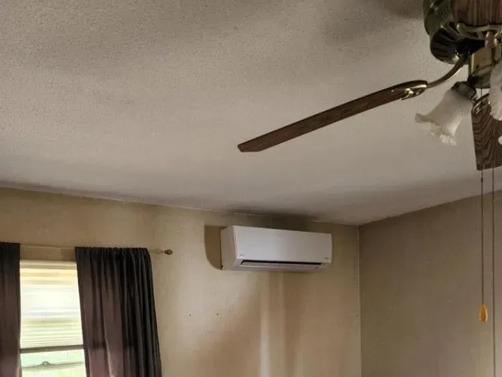 Bedroom wall with a white air conditioner, ceiling fan, and window with dark curtains.