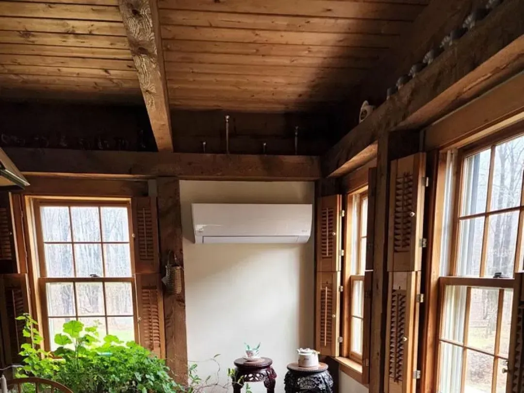 Rustic room with wood beams, window shutters, and a white wall-mounted air conditioner above a small table