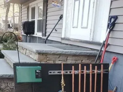 Outdoor plumbing setup with black panel, copper pipes, and tools beside a house porch