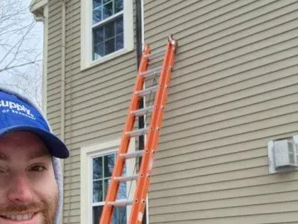 Man in blue cap smiling beside orange ladder against beige house siding