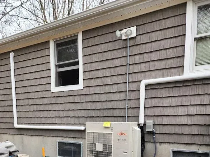 House exterior with gray shingles, window, utility meter, and white conduit mounted on the wall
