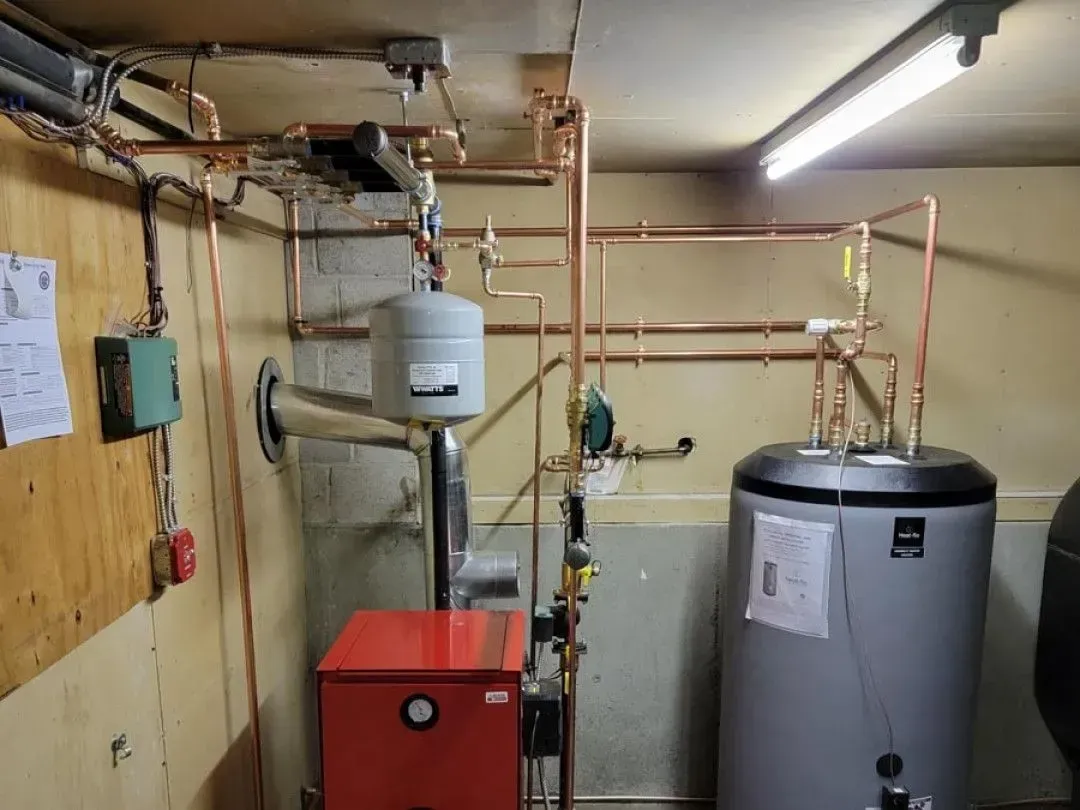 Basement utility room with water heater, red boiler, pipes, and control panels