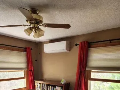 Ceiling fan, white wall AC, and red curtains in a sunlit room with windows