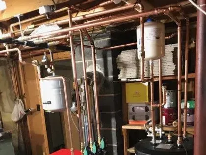 Basement utility room with exposed pipes, water heater, boiler, and storage shelves.