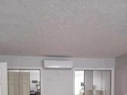 Bedroom with a wall-mounted air conditioner above sliding closet doors and a mirrored wardrobe.