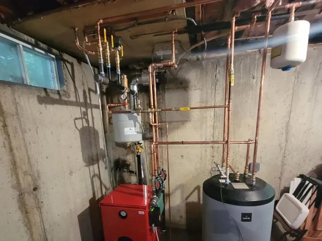 Basement utility room with boiler, water heater, and copper plumbing against a concrete wall