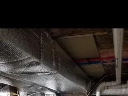 Foil-wrapped ductwork and exposed pipes in a dim ceiling crawlspace