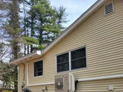 Beige house exterior with windows, siding, utility boxes, and trees in the yard