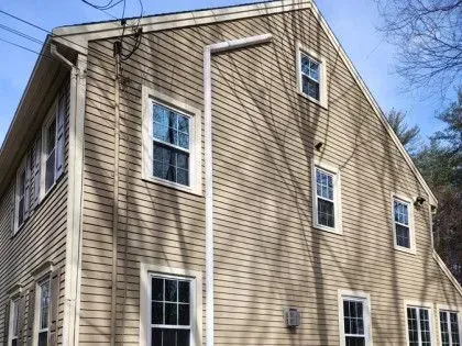 Tan vinyl-sided house exterior with white-trim windows under a clear blue sky
