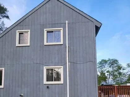 Gray house exterior with two windows and a red fence under a blue sky