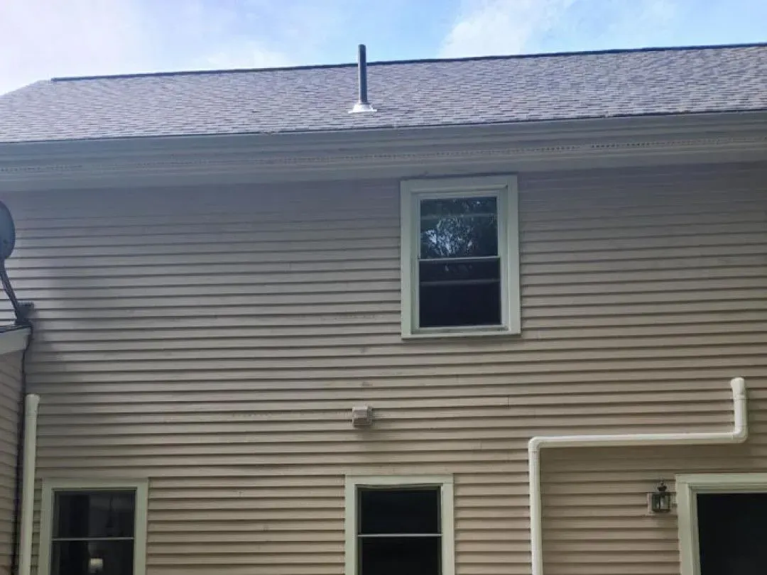 Tan-sided house exterior with two windows, roofline, and white downspout on the right