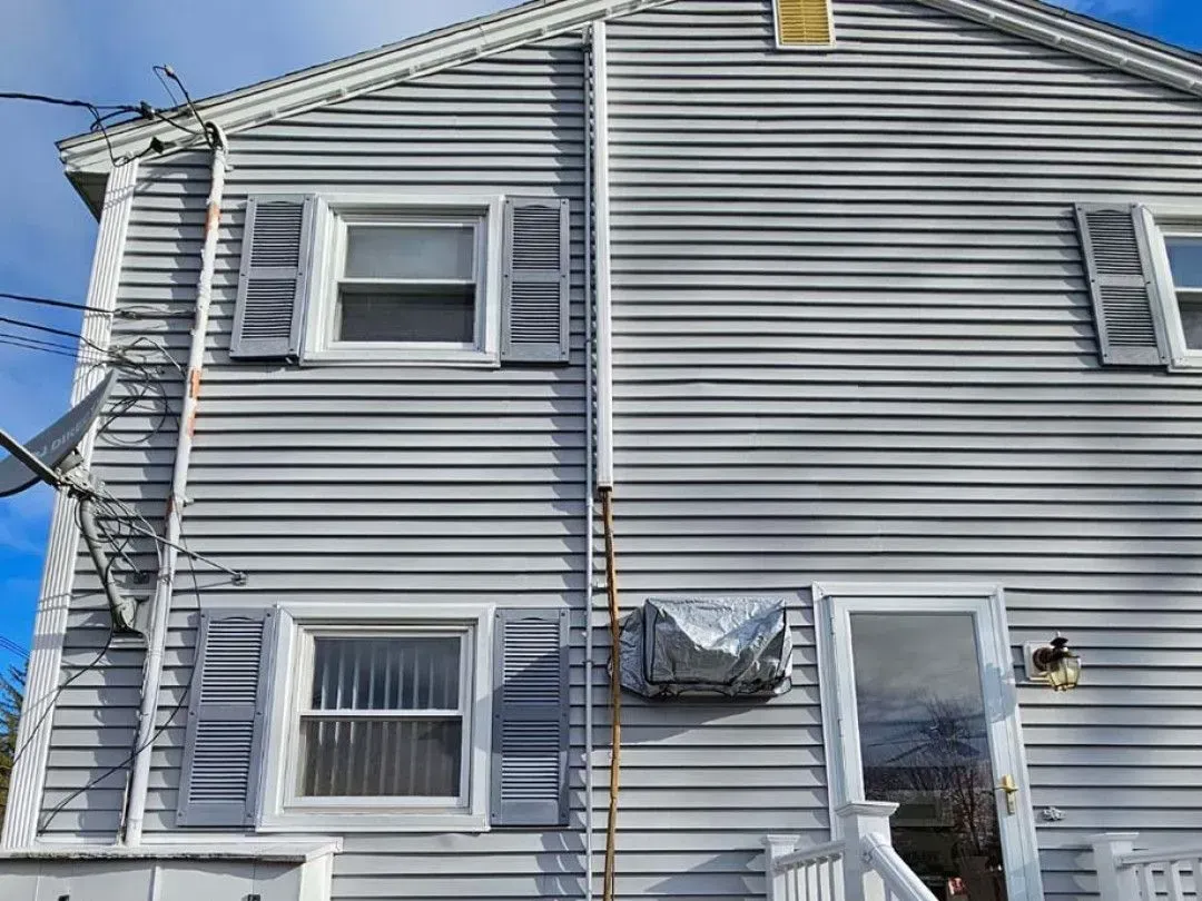 Gray two-story house exterior with white shutters and horizontal siding under a blue sky